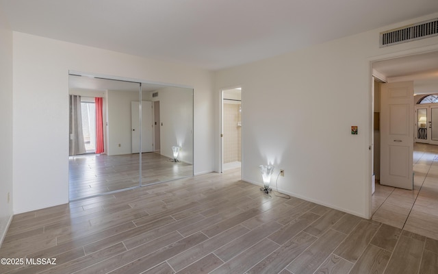 empty room featuring light wood-style floors, baseboards, and visible vents