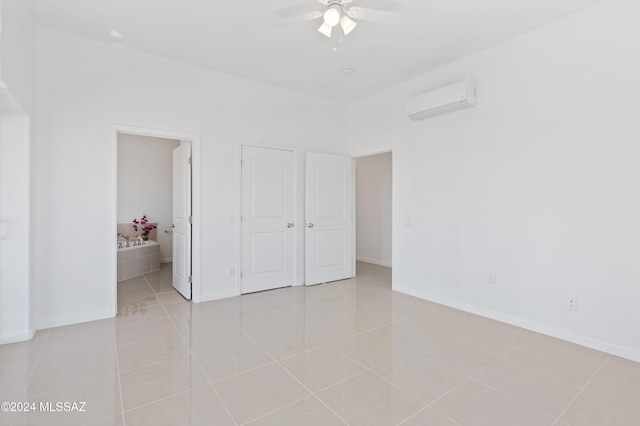 unfurnished bedroom featuring ensuite bath, ceiling fan, light tile patterned flooring, a closet, and an AC wall unit