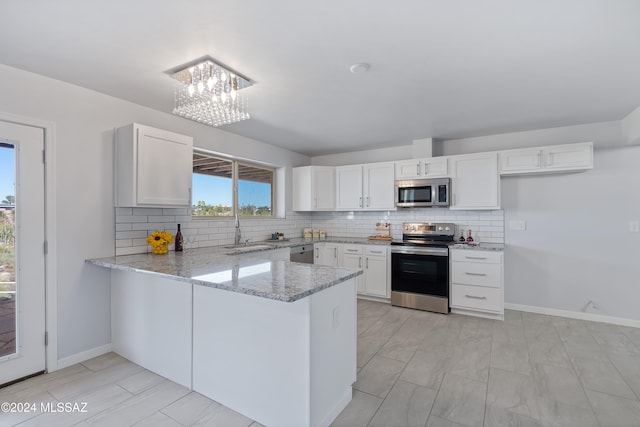 kitchen featuring light stone counters, stainless steel appliances, backsplash, white cabinetry, and kitchen peninsula