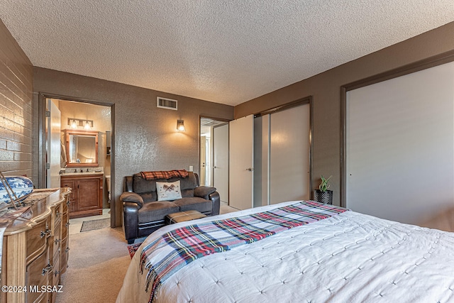 bedroom with light carpet, a textured ceiling, and ensuite bath