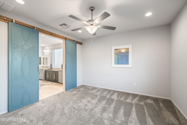 carpeted empty room with a barn door and ceiling fan