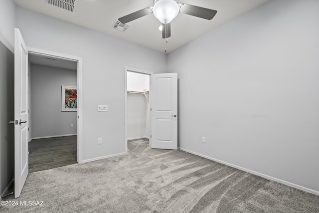 unfurnished bedroom with a closet, a spacious closet, ceiling fan, and carpet floors