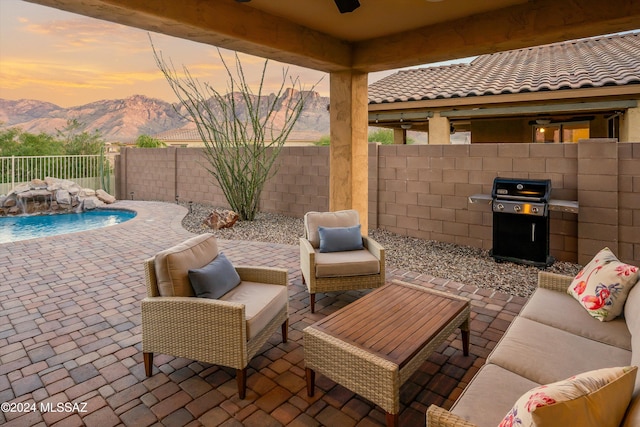 patio terrace at dusk featuring a mountain view, area for grilling, pool water feature, and an outdoor living space