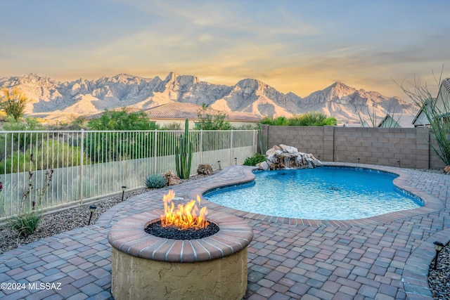 pool at dusk featuring a patio, a fire pit, a mountain view, and pool water feature