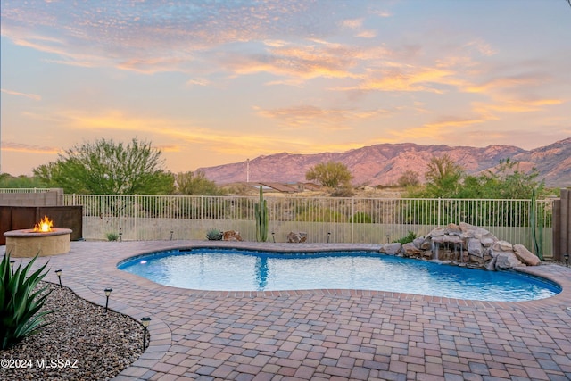 pool at dusk featuring a mountain view, an outdoor fire pit, and a patio