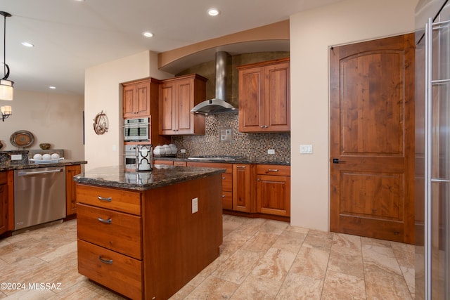 kitchen featuring a center island, wall chimney exhaust hood, hanging light fixtures, dark stone counters, and appliances with stainless steel finishes