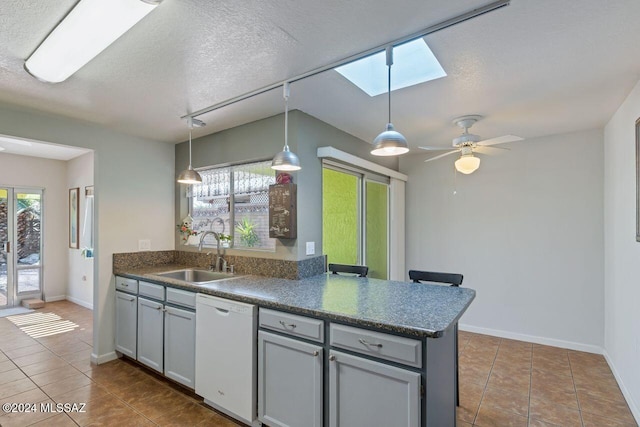 kitchen with kitchen peninsula, decorative light fixtures, white dishwasher, sink, and a skylight