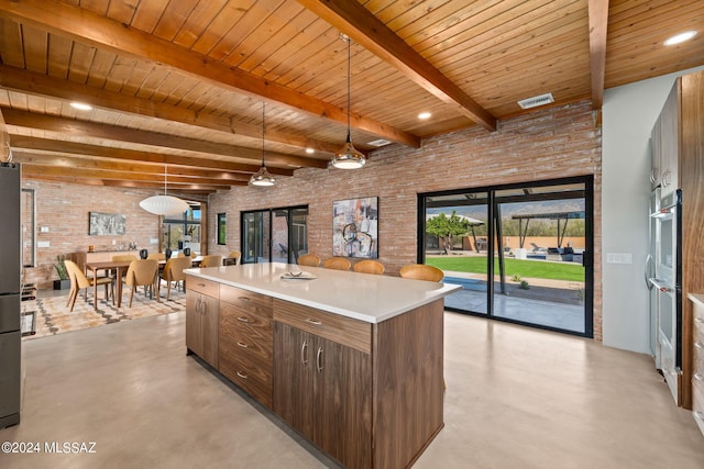 kitchen featuring brick wall, a kitchen island, finished concrete flooring, light countertops, and hanging light fixtures