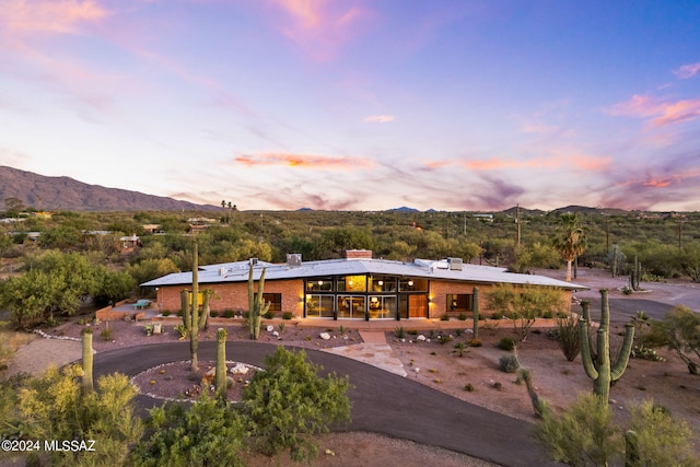 back of house at dusk featuring aphalt driveway, brick siding, and a mountain view