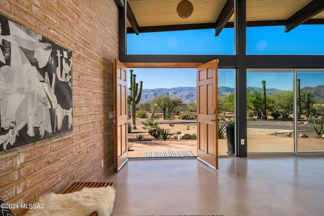 doorway featuring brick wall, beamed ceiling, a mountain view, and finished concrete floors