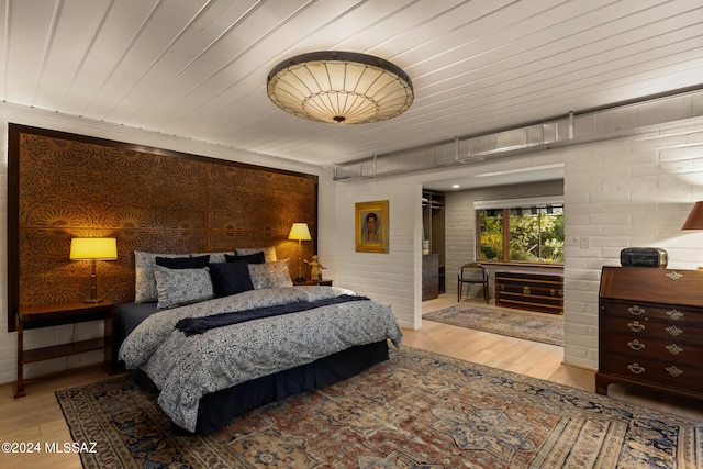 bedroom with light hardwood / wood-style floors, wooden ceiling, and brick wall