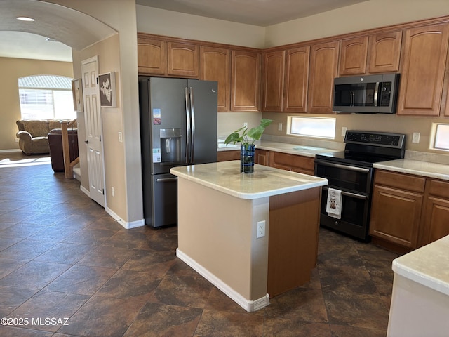 kitchen featuring arched walkways, brown cabinetry, stainless steel appliances, and light countertops