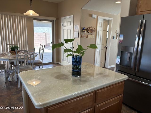 kitchen featuring brown cabinetry, arched walkways, light countertops, stainless steel fridge, and a center island