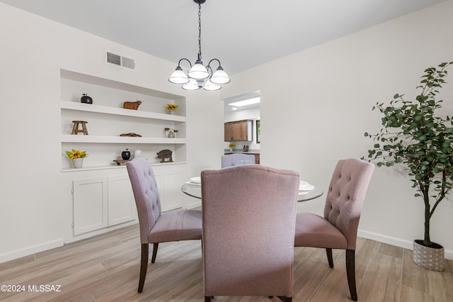 dining area with light hardwood / wood-style floors, a notable chandelier, and built in shelves