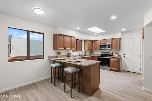 kitchen with a chandelier, appliances with stainless steel finishes, light stone counters, and light wood-type flooring