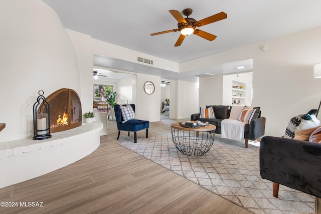 living room with ceiling fan, light wood-type flooring, a fireplace, and built in shelves