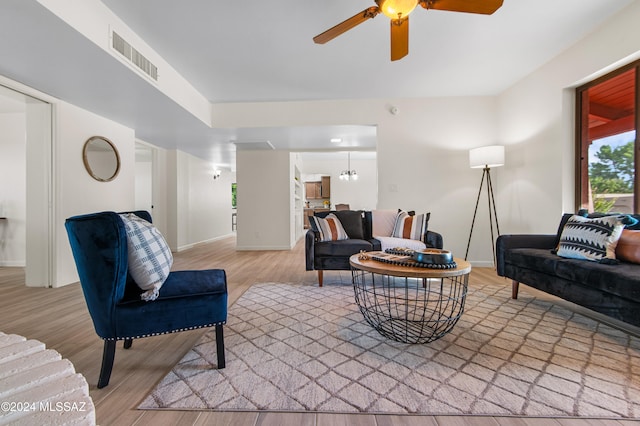 living room with light wood-type flooring and ceiling fan with notable chandelier