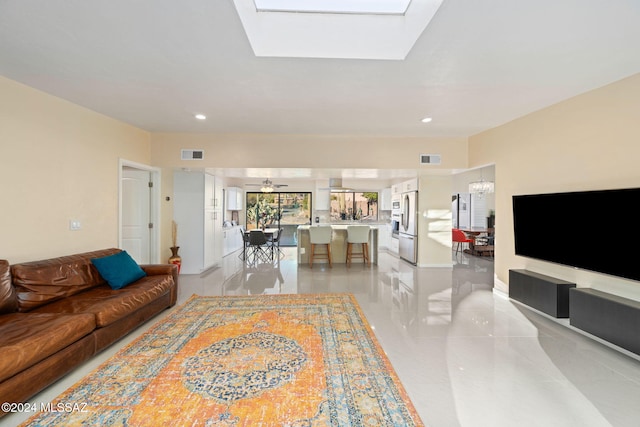 living room with ceiling fan with notable chandelier and a skylight