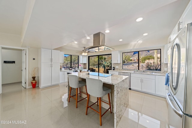 kitchen featuring appliances with stainless steel finishes, light stone counters, a kitchen island, ceiling fan, and white cabinetry