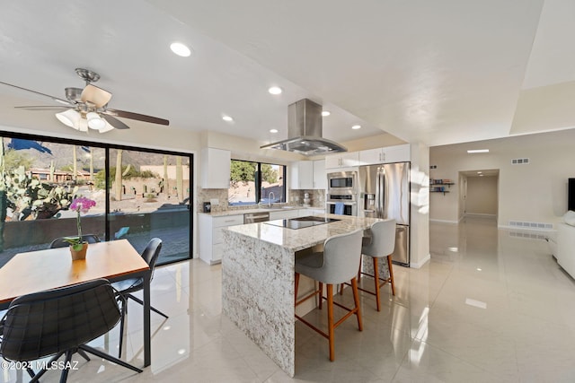 kitchen featuring light stone countertops, tasteful backsplash, white cabinetry, island exhaust hood, and stainless steel appliances