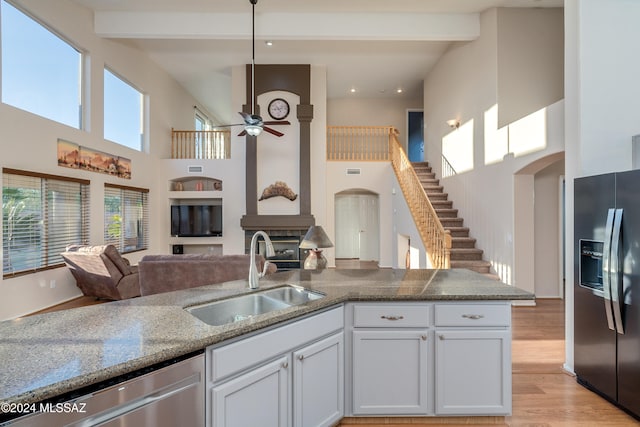 kitchen featuring appliances with stainless steel finishes, a towering ceiling, light wood-type flooring, sink, and white cabinetry