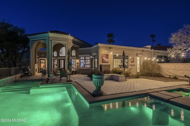 back house at night featuring a patio area and a pool with hot tub