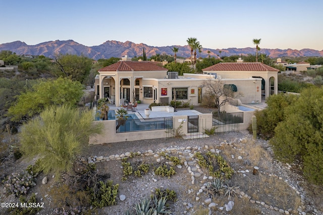 back house at dusk featuring a mountain view and a patio area