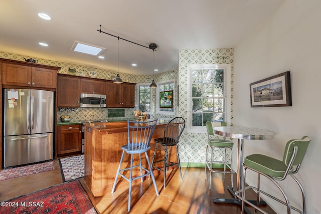 kitchen with pendant lighting, backsplash, stainless steel appliances, a kitchen breakfast bar, and dark hardwood / wood-style flooring