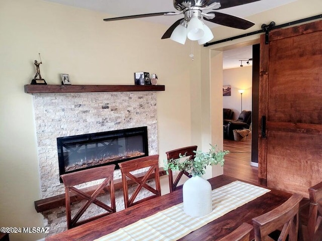 dining space with hardwood / wood-style floors, a barn door, a stone fireplace, and ceiling fan