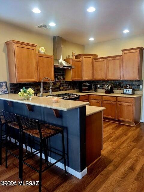 kitchen with decorative backsplash, wall chimney exhaust hood, kitchen peninsula, and dark hardwood / wood-style floors