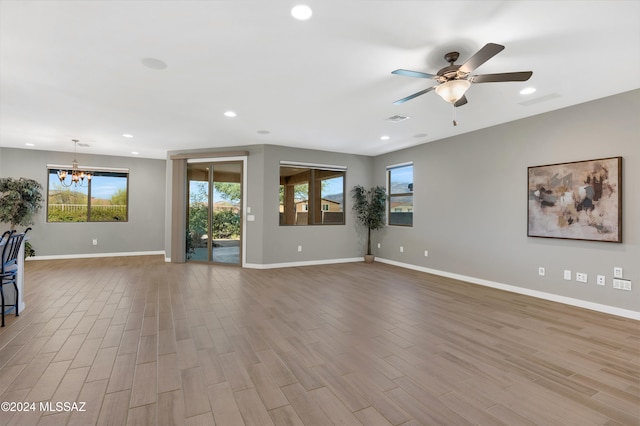 unfurnished living room with ceiling fan with notable chandelier, plenty of natural light, and light hardwood / wood-style floors