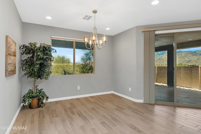 spare room featuring light wood-type flooring, a notable chandelier, and a healthy amount of sunlight