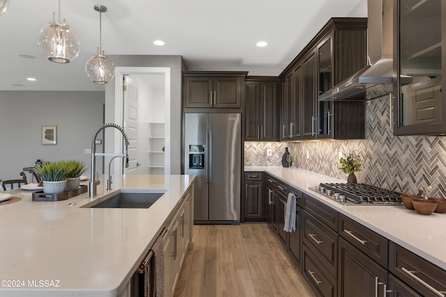 kitchen featuring sink, appliances with stainless steel finishes, wall chimney exhaust hood, hanging light fixtures, and light wood-type flooring