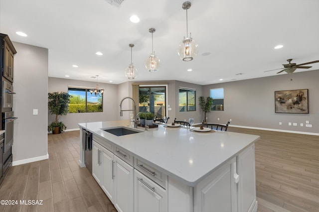 kitchen featuring a kitchen island with sink, sink, decorative light fixtures, and white cabinets