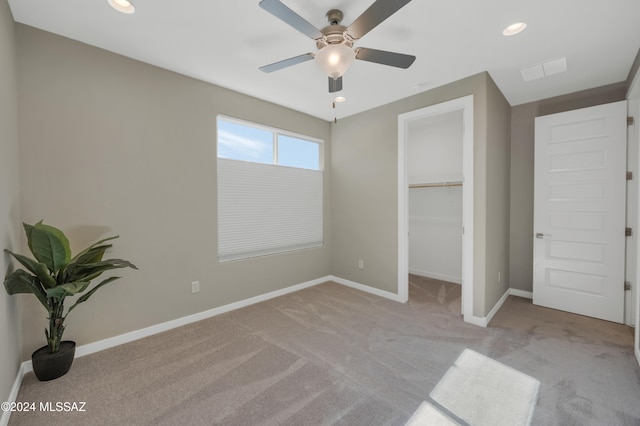 unfurnished bedroom with a closet, a spacious closet, light carpet, and ceiling fan