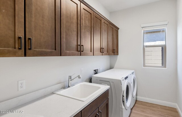 laundry room with cabinets, independent washer and dryer, sink, and light hardwood / wood-style flooring