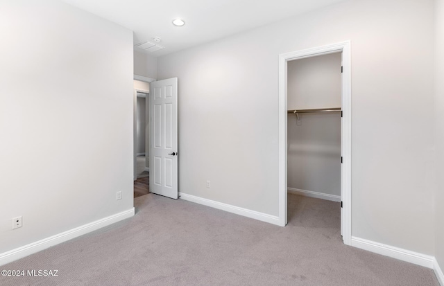 unfurnished bedroom featuring a walk in closet, light carpet, and a closet