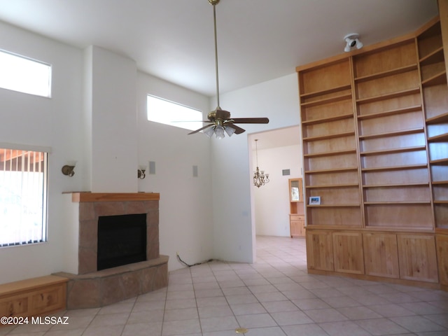 unfurnished living room featuring a towering ceiling, light tile patterned flooring, a fireplace, and ceiling fan