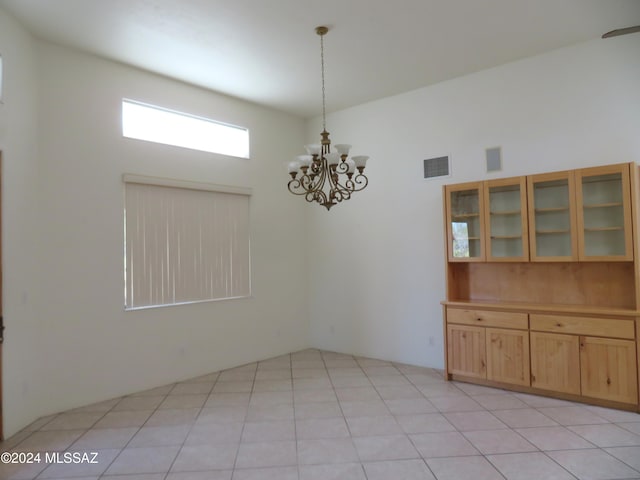 unfurnished dining area with a towering ceiling, light tile patterned flooring, and a chandelier