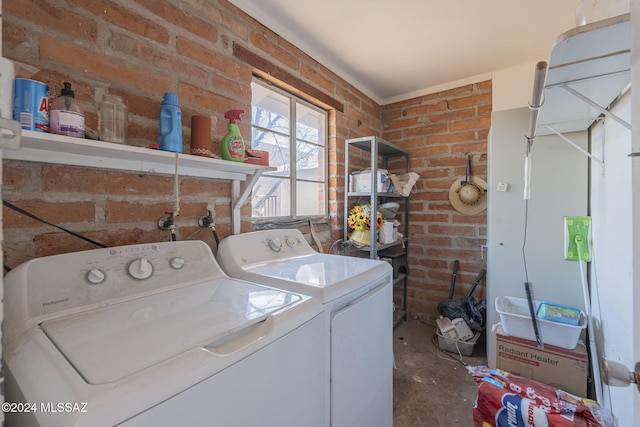 clothes washing area with washer and clothes dryer and brick wall