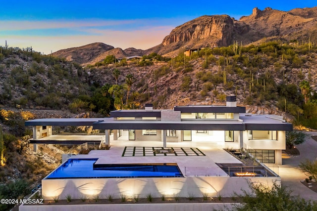 back house at dusk featuring a mountain view, a patio, and a fire pit