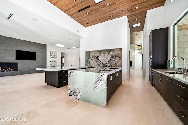 kitchen with dark brown cabinetry, sink, a spacious island, a tile fireplace, and tile walls