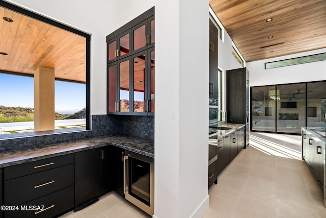 kitchen with beverage cooler, backsplash, wooden ceiling, and dark stone countertops