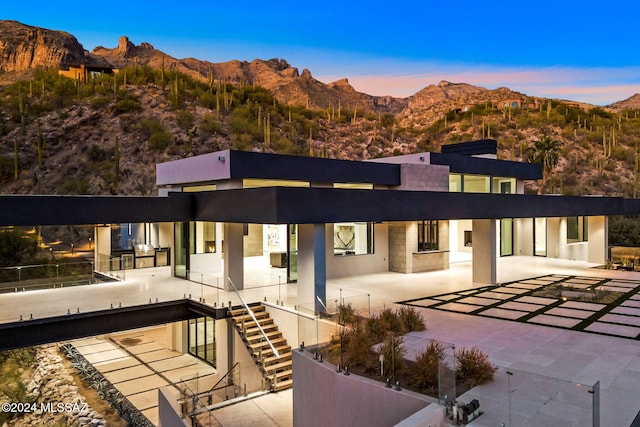 back house at dusk featuring a mountain view and a patio