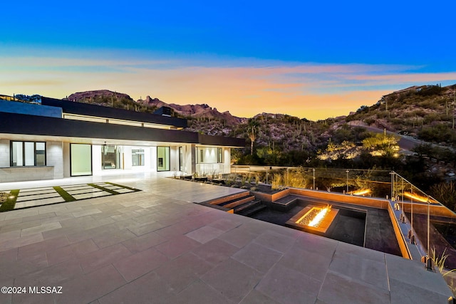 pool at dusk with a mountain view, an outdoor fire pit, and a patio area