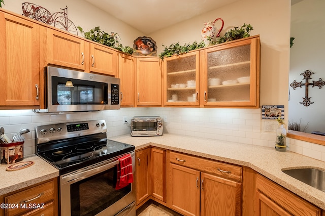 kitchen with decorative backsplash, appliances with stainless steel finishes, sink, and light stone counters