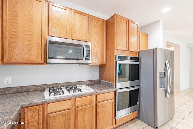 kitchen with light tile patterned floors, appliances with stainless steel finishes, and dark countertops