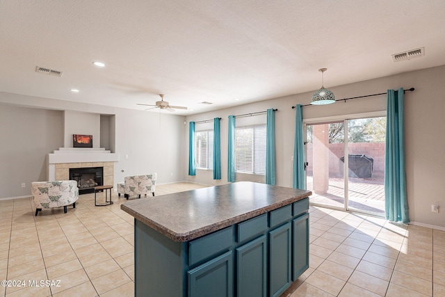 kitchen with a fireplace, light tile patterned floors, dark countertops, visible vents, and a kitchen island