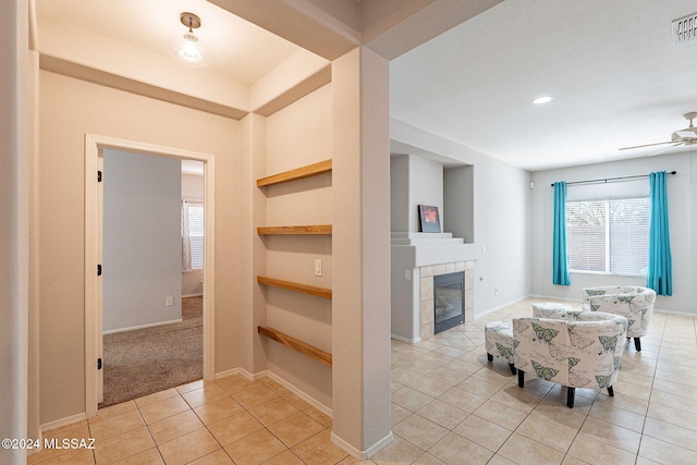 unfurnished living room with built in features, light tile patterned floors, visible vents, ceiling fan, and a tile fireplace