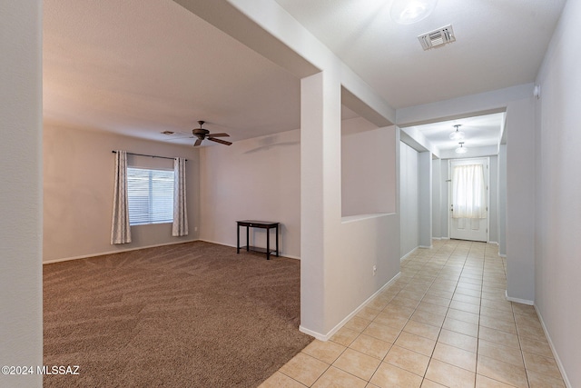 corridor featuring light colored carpet, visible vents, baseboards, and light tile patterned flooring